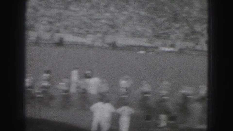 Soft, motion-blurred 8mm frame of football players and sideline figures during a 1975 Harrisburg school game.