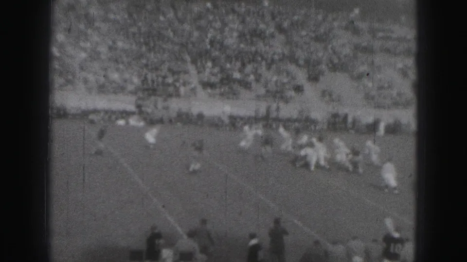Wide 1975 Harrisburg football-game view with players on the field, sideline figures, and packed bleachers in the background.