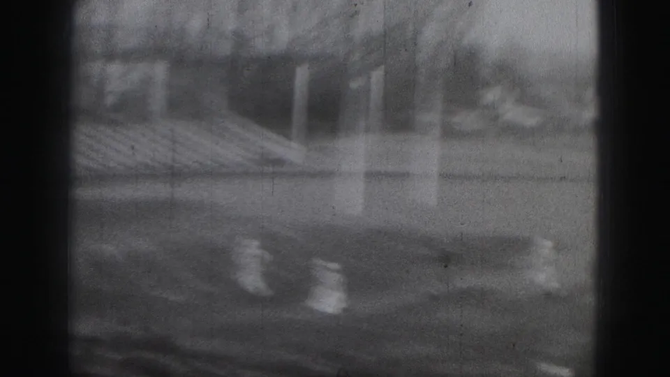 Black-and-white 8mm frame from the Harrisburg football game, showing players near the goalpost and stadium seating beyond.