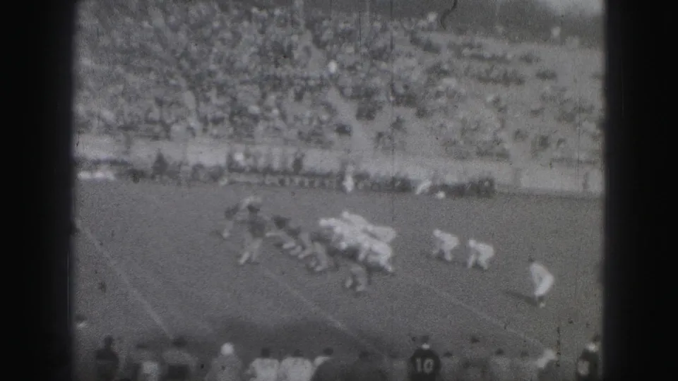 1975 Harrisburg football frame showing a line of scrimmage from the stands, with spectators filling the bleachers.