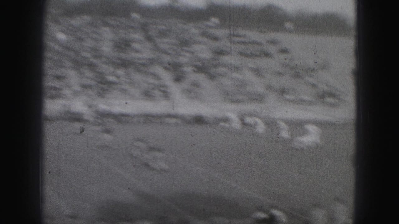 Distant football field and packed bleachers seen through dark film-frame edges.