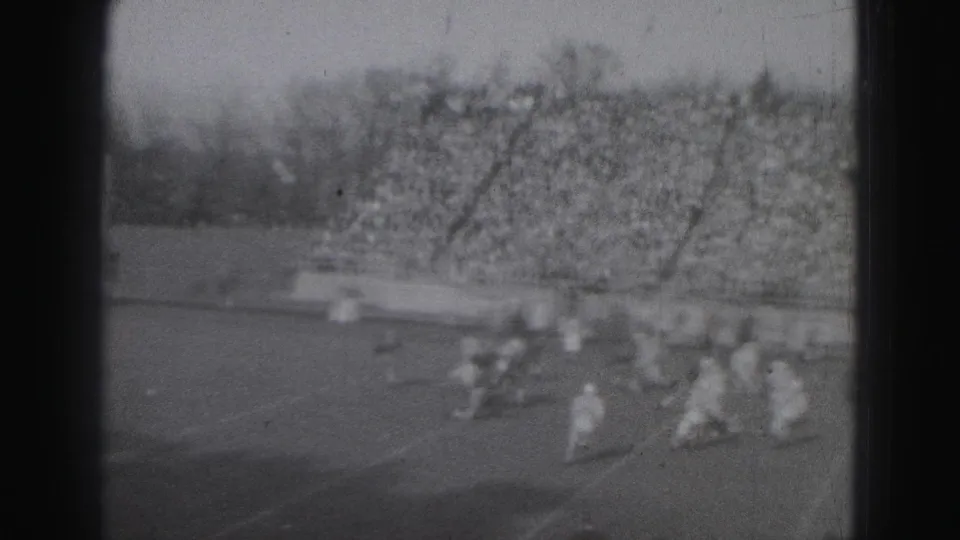 1975 Harrisburg football scene with clustered players near the sideline and a dense crowd filling the bleachers.