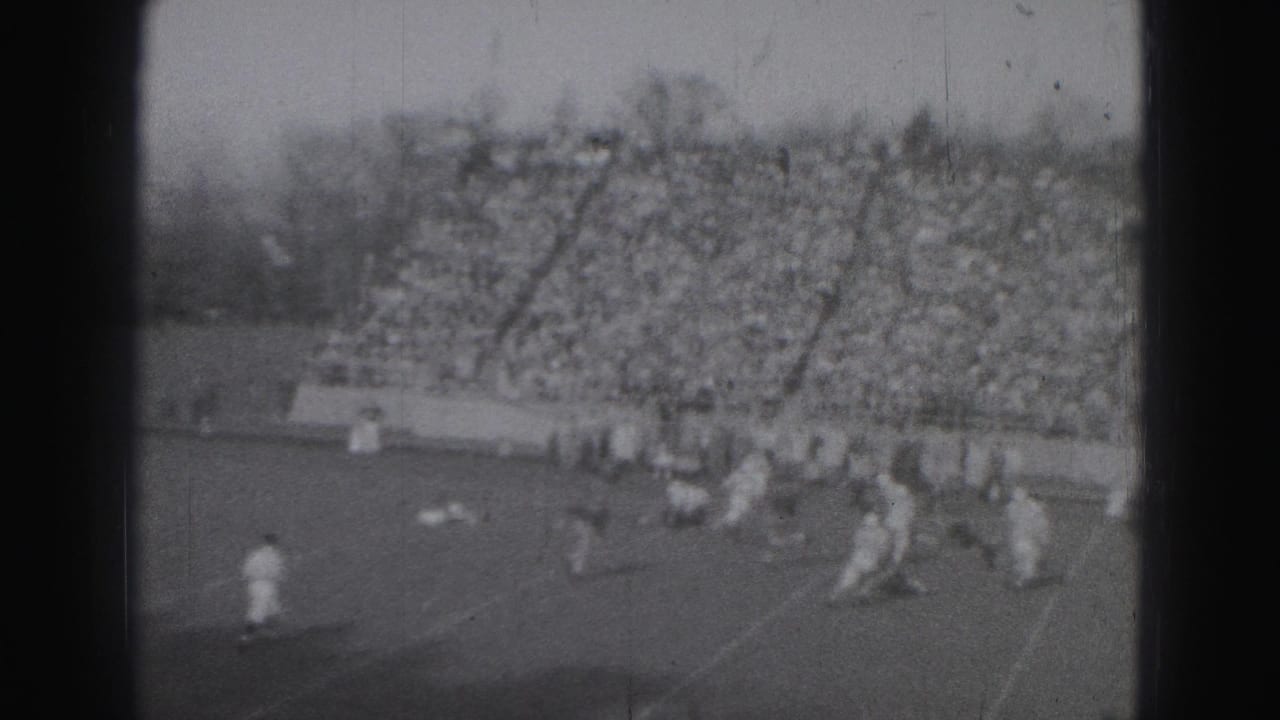Football players on a field before a large crowd in bleachers.
