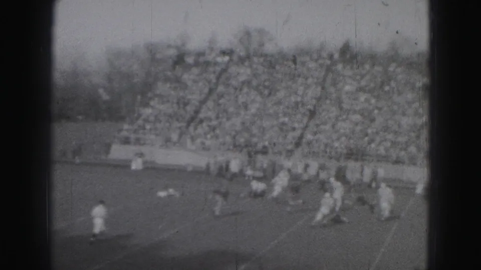 1975 Harrisburg 8mm footage showing football players clustered on the field with packed bleachers behind them.