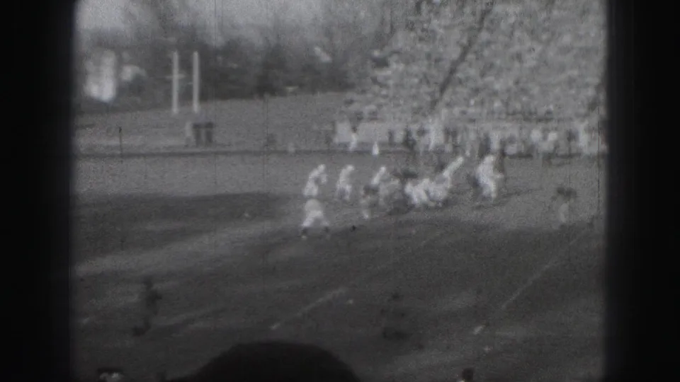 Harrisburg football action on 8mm film, with players in light uniforms moving across the field near visible goalposts.