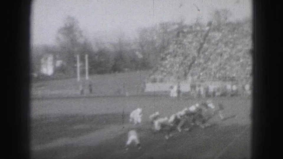 1975 Harrisburg home-movie frame showing a football play breaking toward the sideline with players falling or tackling near the crowd.