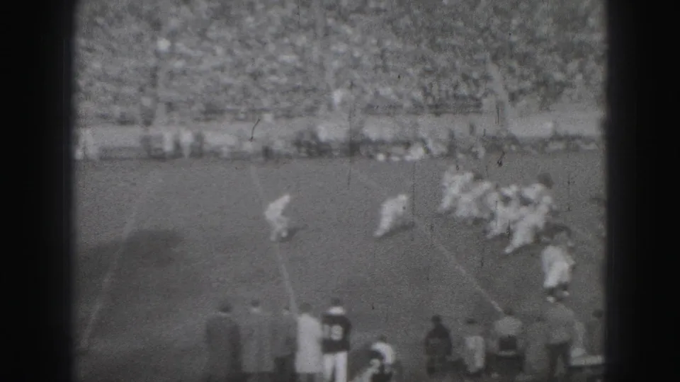 1975 Harrisburg football action near the sideline, with players set on the marked field and spectators packed in the background.