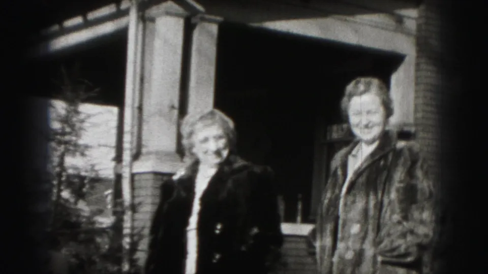 Two women stand near a brick residential porch in the final 1975 Harrisburg home-movie frame.