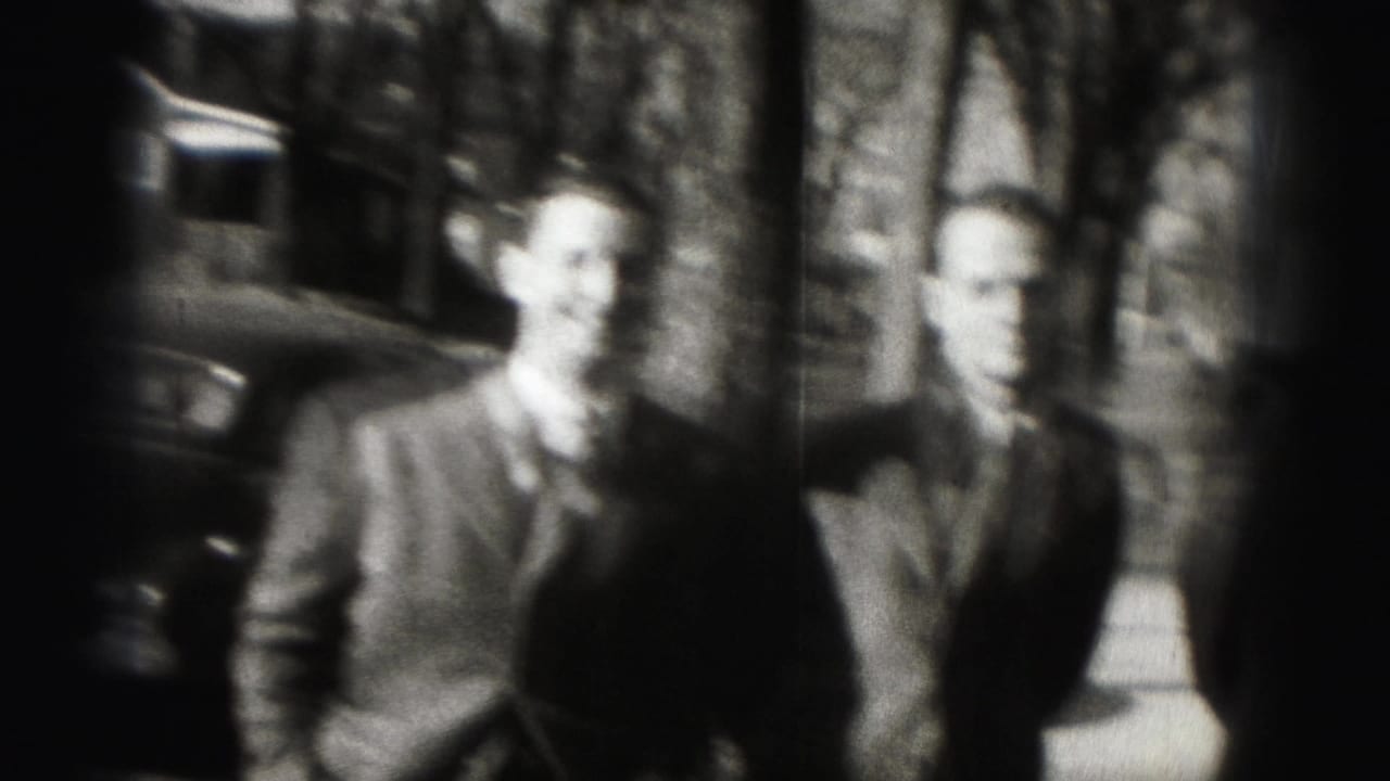Two suited adult men are seen in soft focus on a Harrisburg sidewalk, with trees and a parked car in the background.