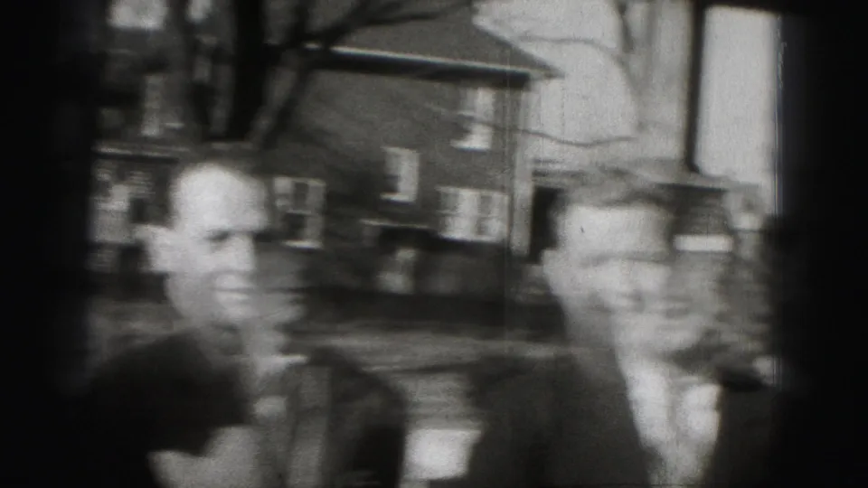 Two adult men in suits appear on a residential Harrisburg street in grainy 1975 8mm footage.