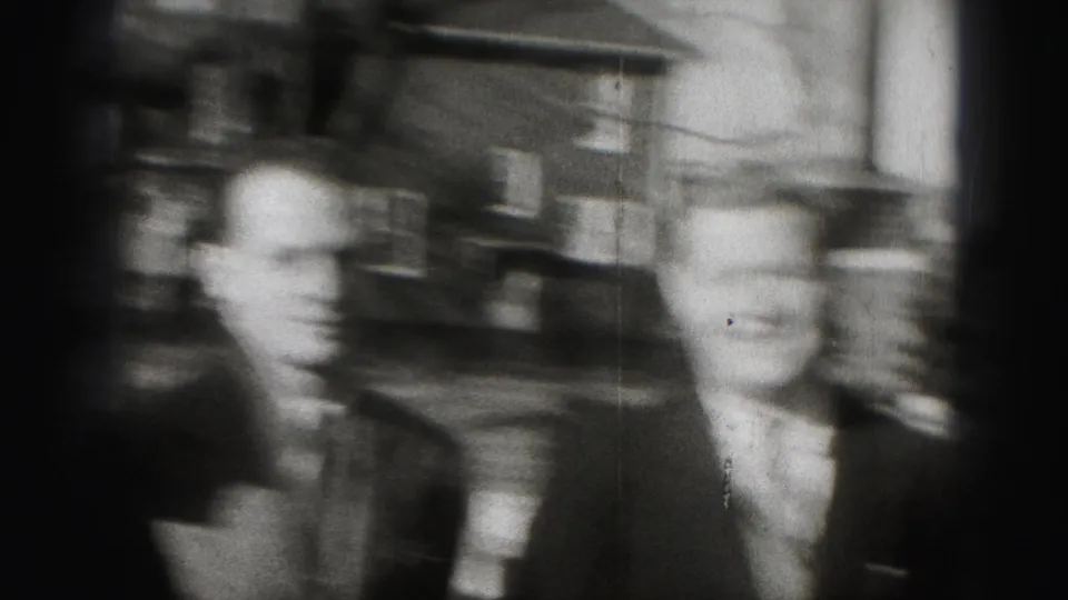 Two men in suits and ties stand beside a residential street, with Harrisburg location supported by clip metadata.