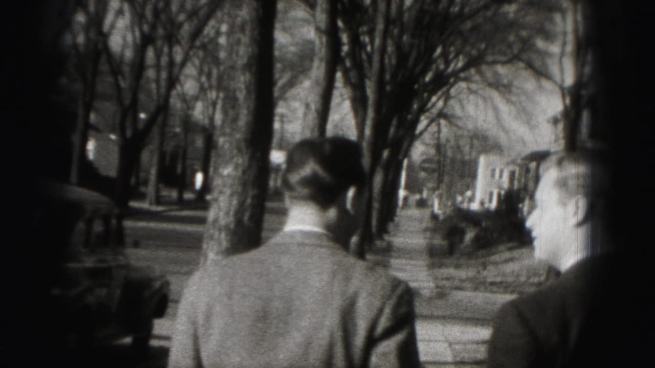 Two adult men in suits walk away from the camera along a tree-lined Harrisburg sidewalk in 1975 home-movie footage.