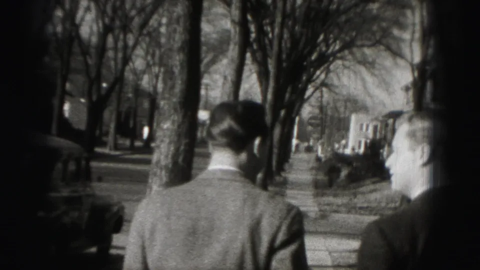 Two adult men in suits walk away from the camera along a tree-lined Harrisburg sidewalk in 1975 home-movie footage.