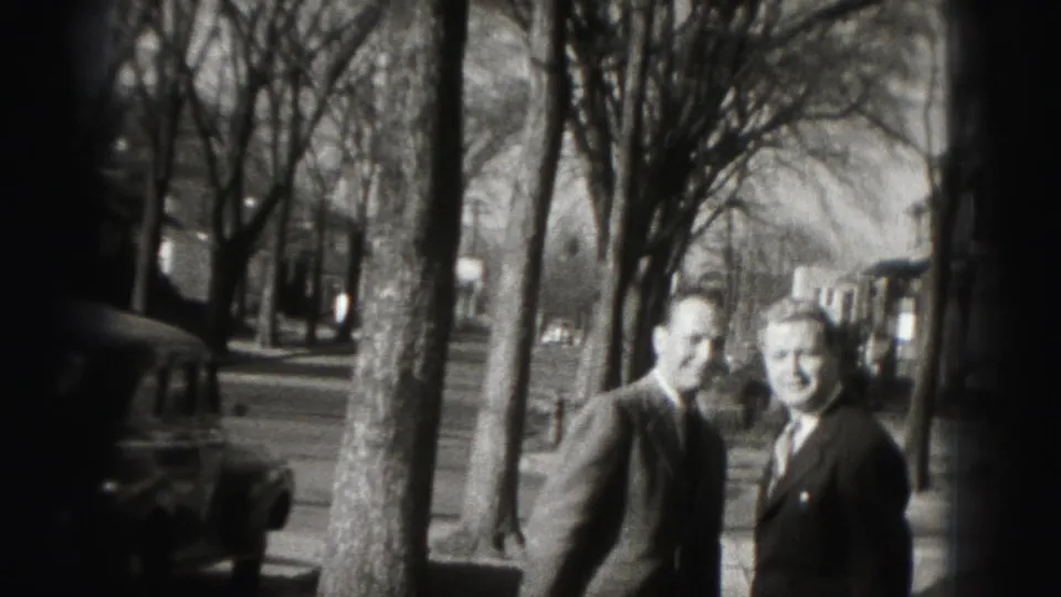 The two suited men turn back toward the camera and smile on a Harrisburg sidewalk in 1975 home-movie footage.