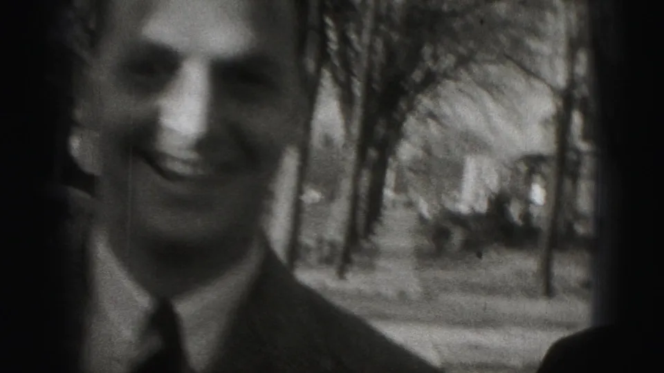A close, soft-focus view shows a smiling adult man in a suit during the Harrisburg sidewalk scene.