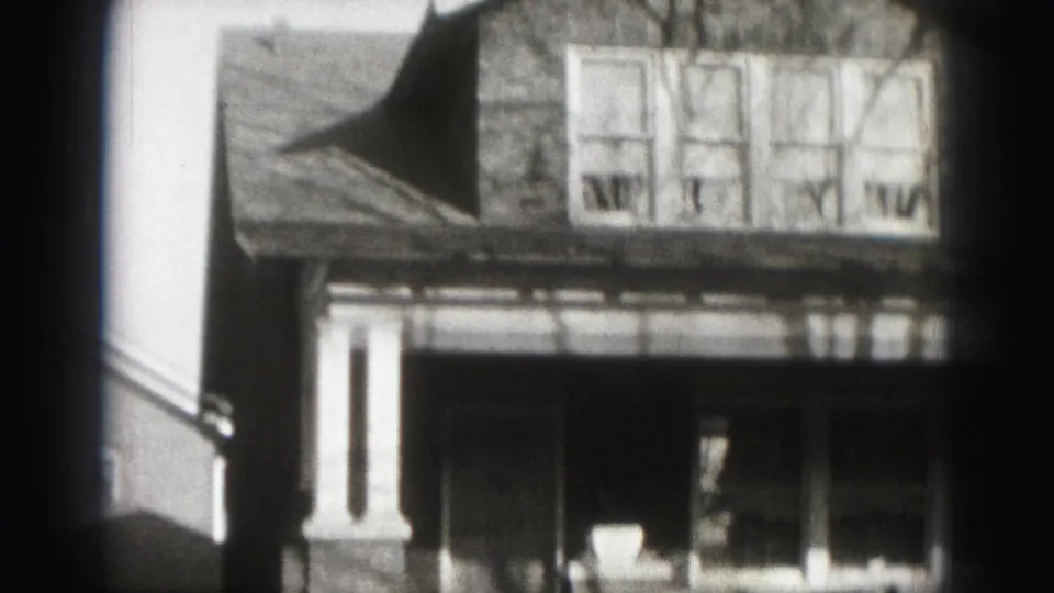 1975 Harrisburg home-movie frame showing a two-story suburban house facade with porch, brickwork, and four upper windows.