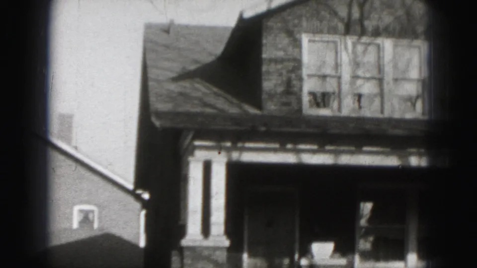1975 Harrisburg frame showing a partial suburban house exterior with upper windows, porch area, and adjacent building wall.