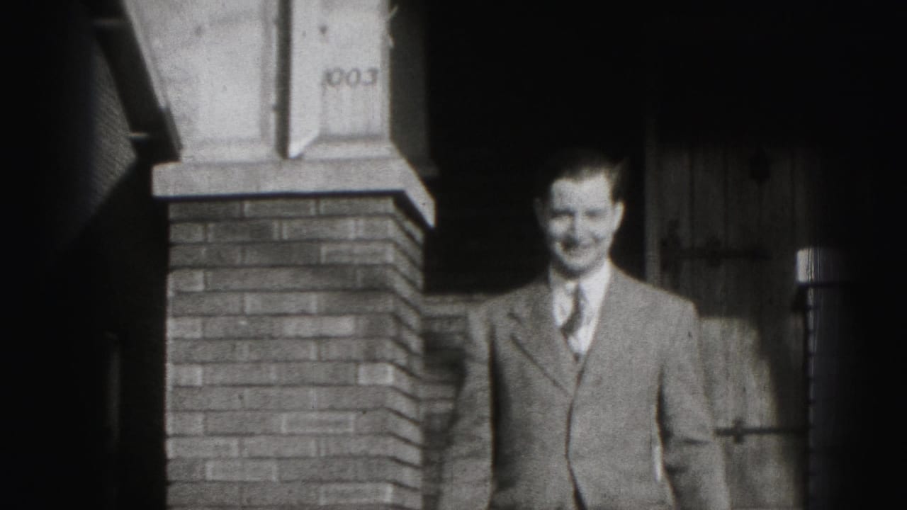 Man in a suit walks near a brick porch and house entry.