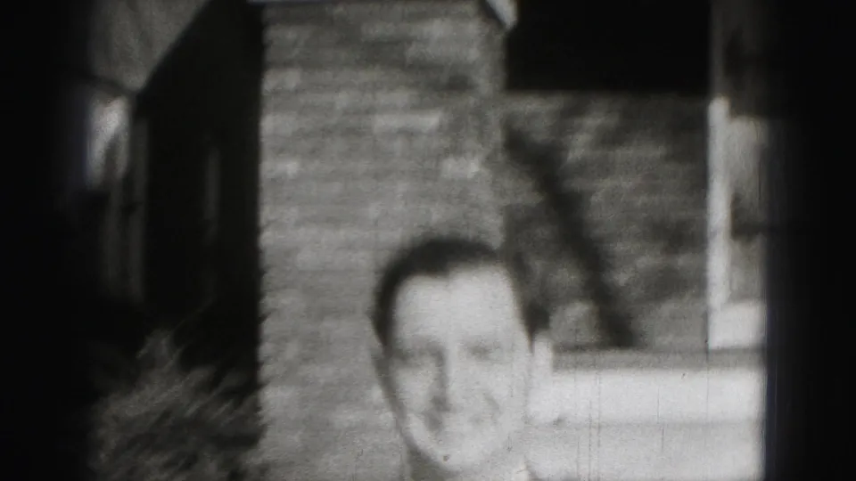 A soft-focus close view shows the suited man smiling near the brick exterior of the Harrisburg house.