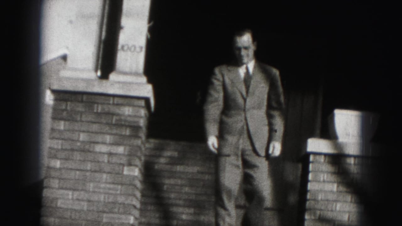 In 1975 Harrisburg home-movie footage, a suited man appears in a doorway framed by brick porch columns.