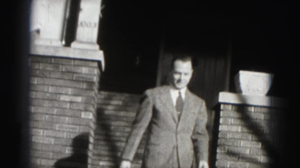 The Harrisburg 8mm frame shows a smiling suited man moving toward the camera from a brick entryway.