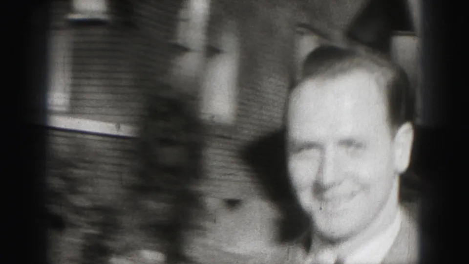 The final Harrisburg home-movie frame is a soft, blurred close-up of the smiling suited man near the camera.