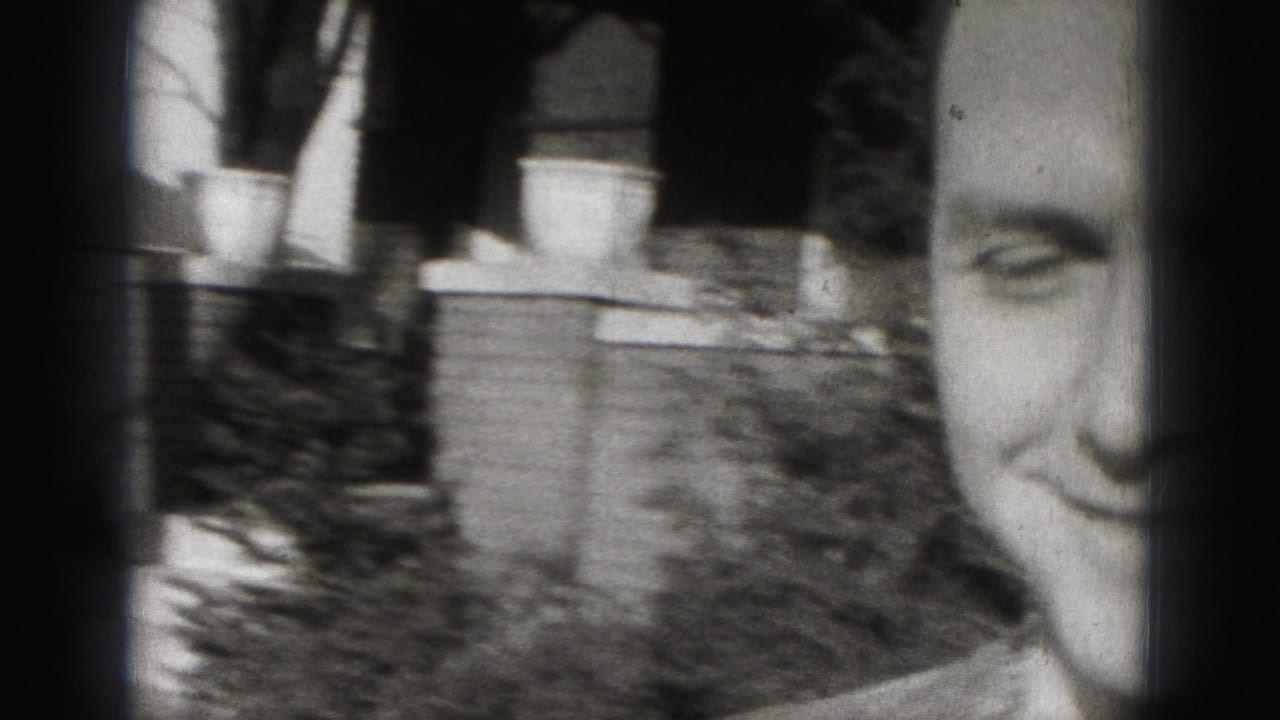 Man smiling close to the camera beside a tree and residential yard.