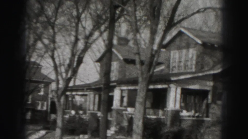 Two-story Harrisburg house exterior with front porch columns, peaked rooflines and leafless trees, filmed in 1975.