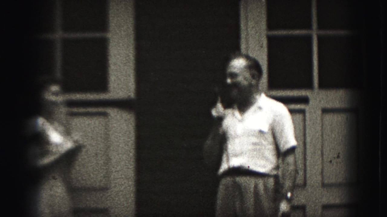 In 1975 Harrisburg home-movie footage, a man with a microphone stands by paneled doors as a girl moves near the left edge.