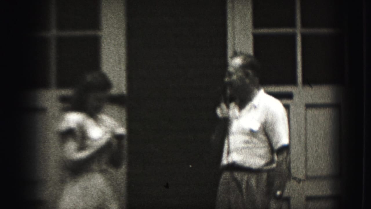 A girl and a man with a handheld microphone stand outside a Harrisburg house in grainy 1975 8mm footage.