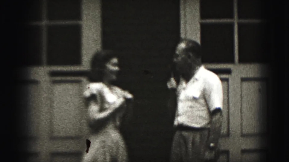 The girl stands nearer to the man holding the microphone outside the Harrisburg house, framed by doors and windows.