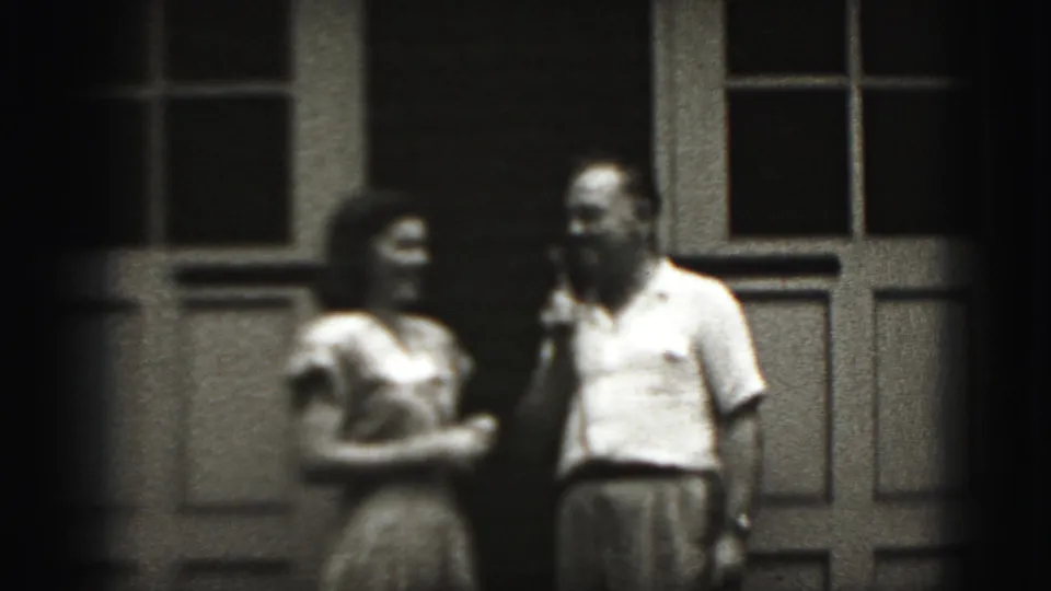 The man appears to gesture as the woman stands beside him outside the paneled building in 1975 Harrisburg home-movie footage.