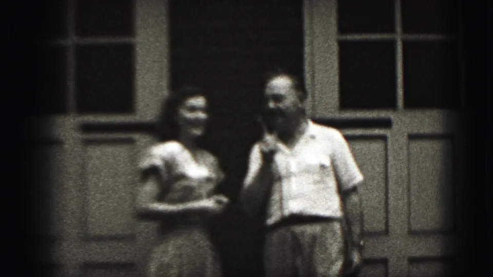 A woman appears to smile while standing beside a man outside a paneled doorway in the 1975 Harrisburg 8mm clip.