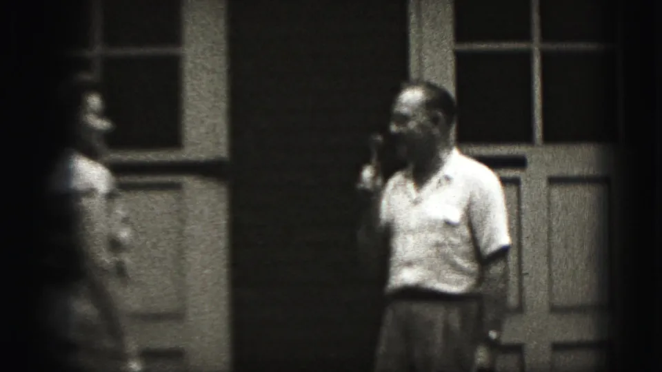 The woman moves into view from the left as the man holding the microphone turns toward her on the Harrisburg porch.