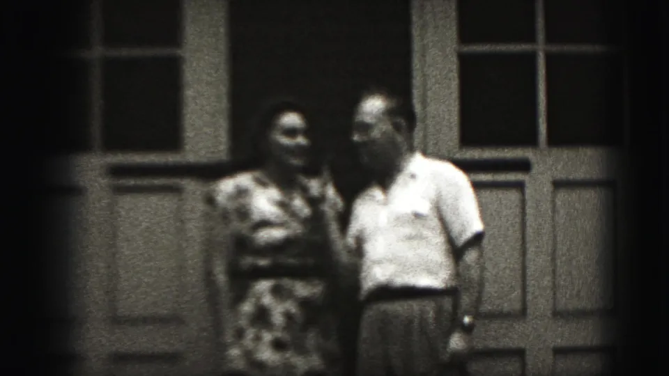 The woman and man remain close together before a paneled doorway in soft 8mm footage from the Harrisburg home-movie clip.