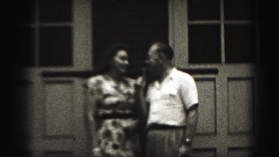 The couple appears to converse on a Harrisburg porch in 1975, with the woman in a patterned dress and the man in a light shirt.