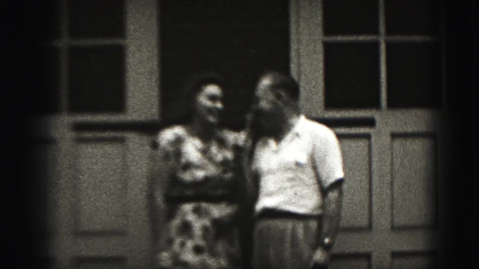 A 1975 Harrisburg home-movie frame shows the couple close together on a porch, with soft focus and visible film grain.