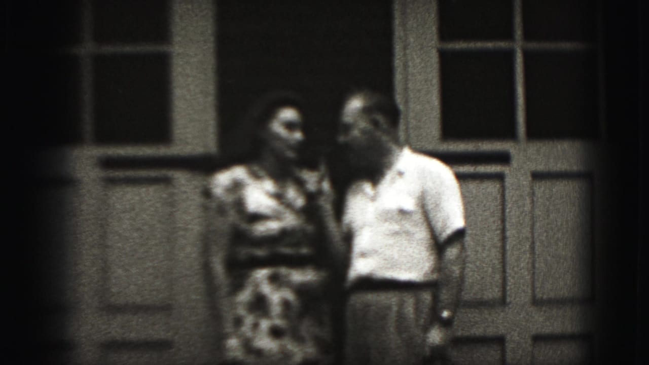 Man holding a microphone stands close to a woman outside paneled doors.