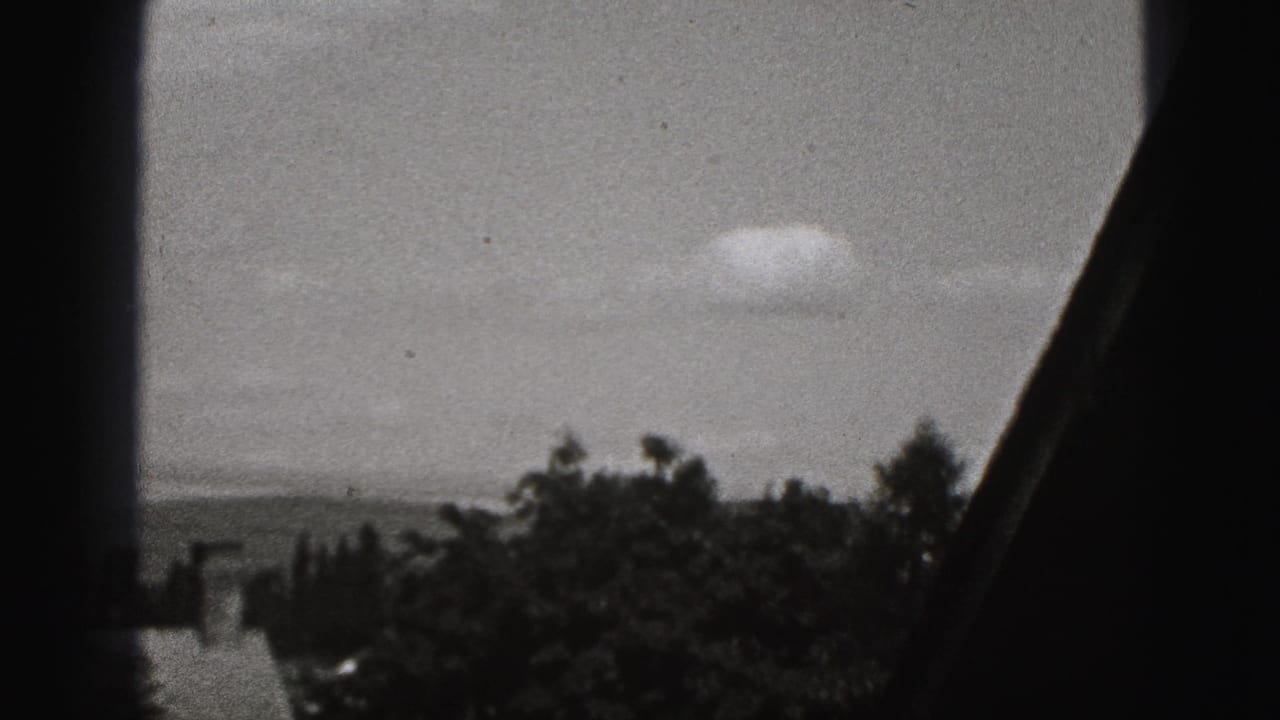 Window-framed view of cloudy sky, distant trees, and a dark interior edge.