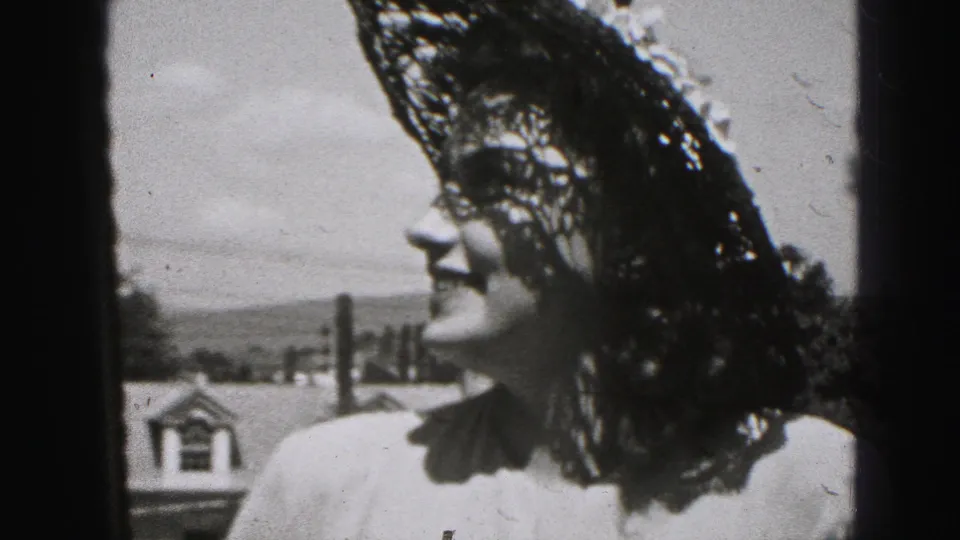 Profile-like close-up of the same young woman smiling in a lace hat, with sky, rooftops, and distant trees behind her.