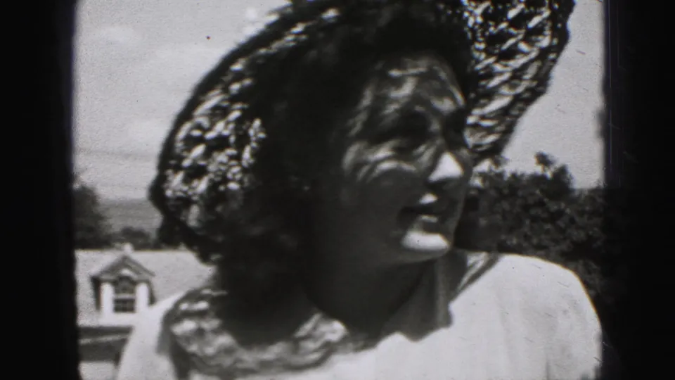 A woman in Harrisburg, Pennsylvania home-movie footage wears a wide lace hat and light dress, her face partly shadowed as she looks left.