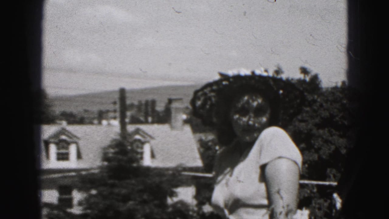 1975 Harrisburg home-movie frame showing a woman in a large dark hat making a face near residential rooftops and trees.