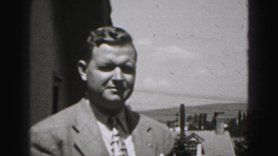 1975 Harrisburg home-movie frame of a man in a suit facing the camera in a residential outdoor setting.