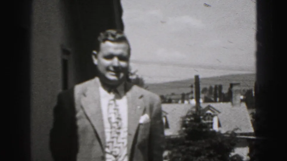 The suited man remains near the building edge, smiling toward the camera with Harrisburg residential rooftops behind him.