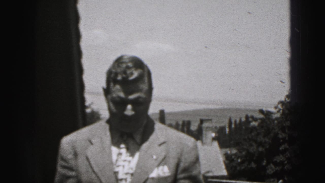Man in a suit stands at a distance within a dark 8mm frame border.