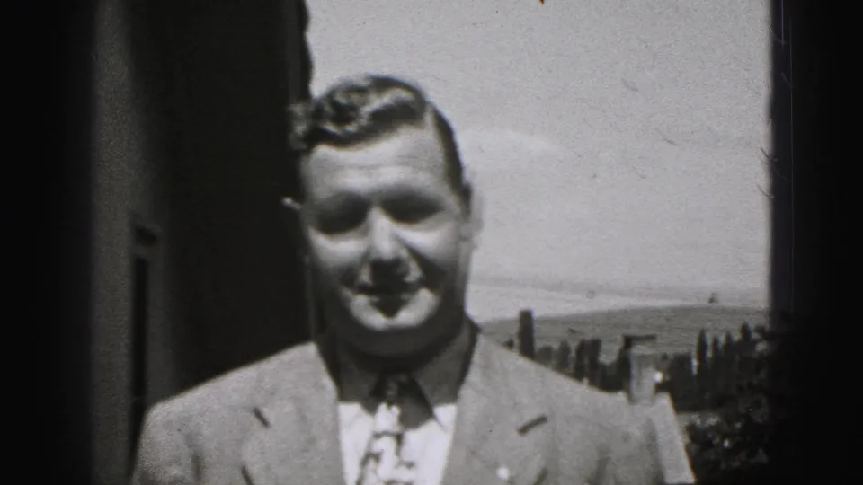 The suited man approaches the camera in the 1975 Harrisburg home-movie footage, with landscape and sky visible behind him.