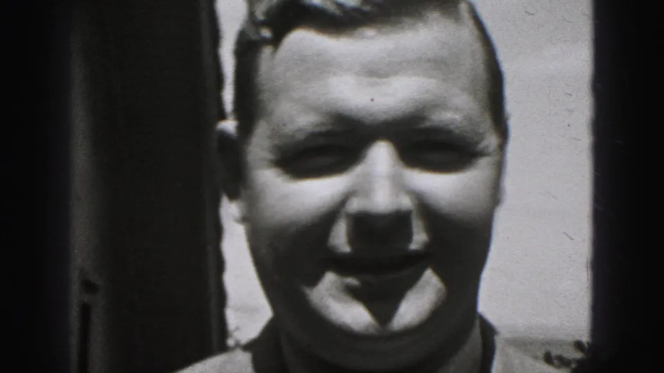 Smiling man shown in close-up in the 1975 Harrisburg home-movie clip, framed tightly with bright outdoor light and dark side borders.