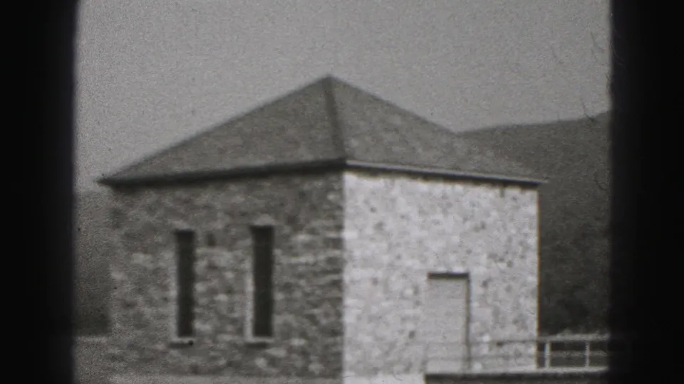 A square stone waterside building with a triangular roof appears in the 1975 Harrisburg home-movie scene, framed by railings and hills.