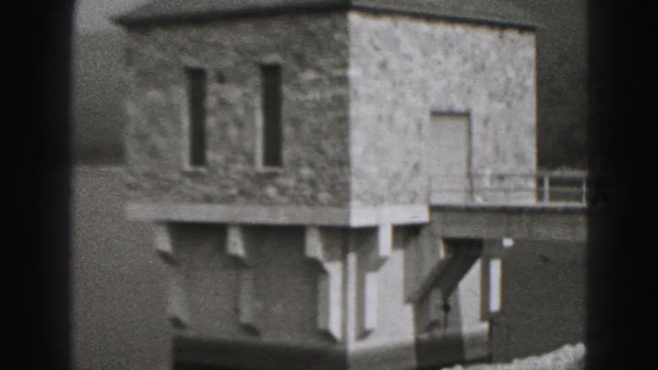 The frame shows the stone waterside building and adjacent light-colored structure over a walkway, consistent with the 1975 Harrisburg lake scene.