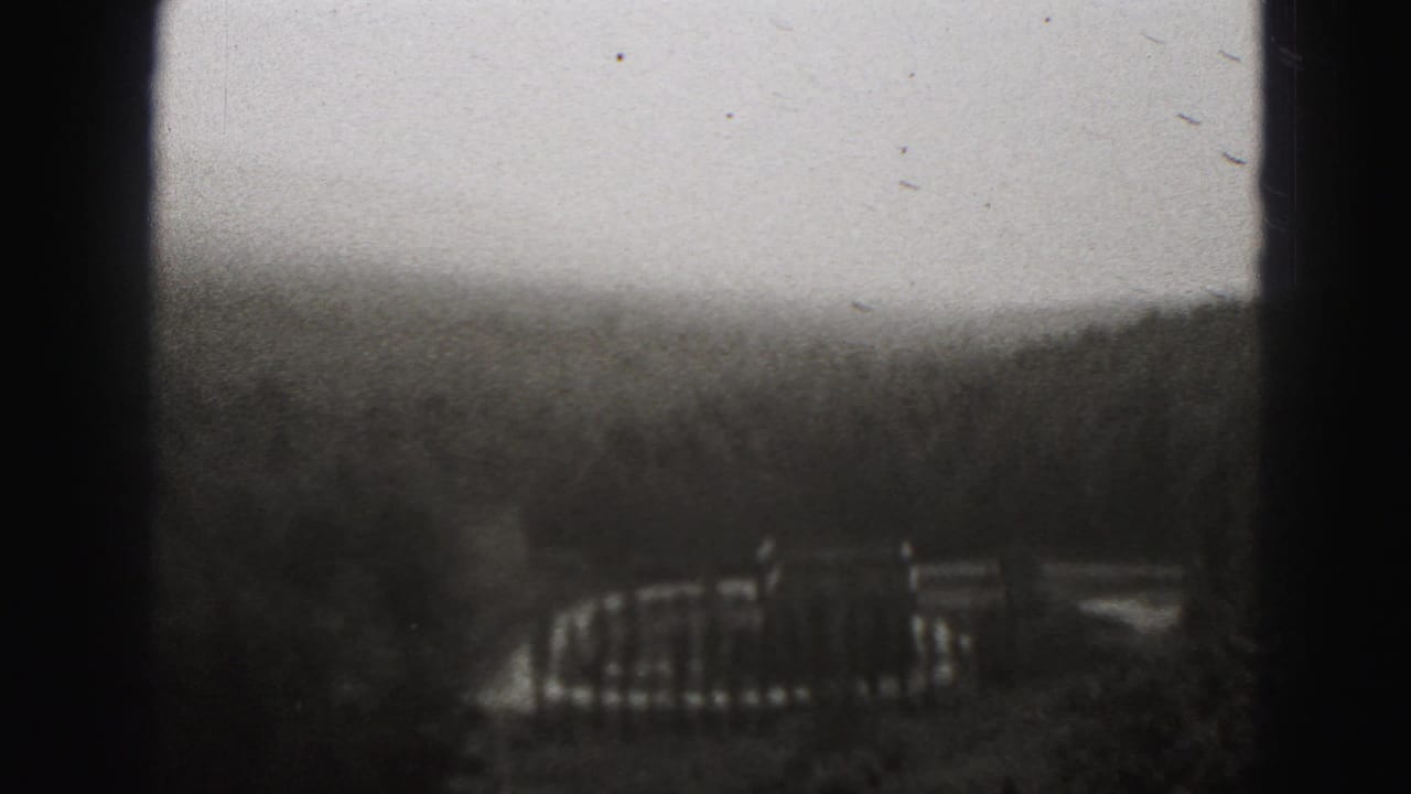 Hazy wooded hillside with distant structures seen through dark 8mm frame borders.
